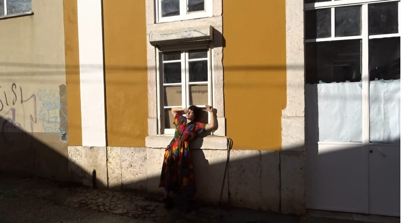 Juliana Fernandes leaning against a sunlit window in a colourful dress