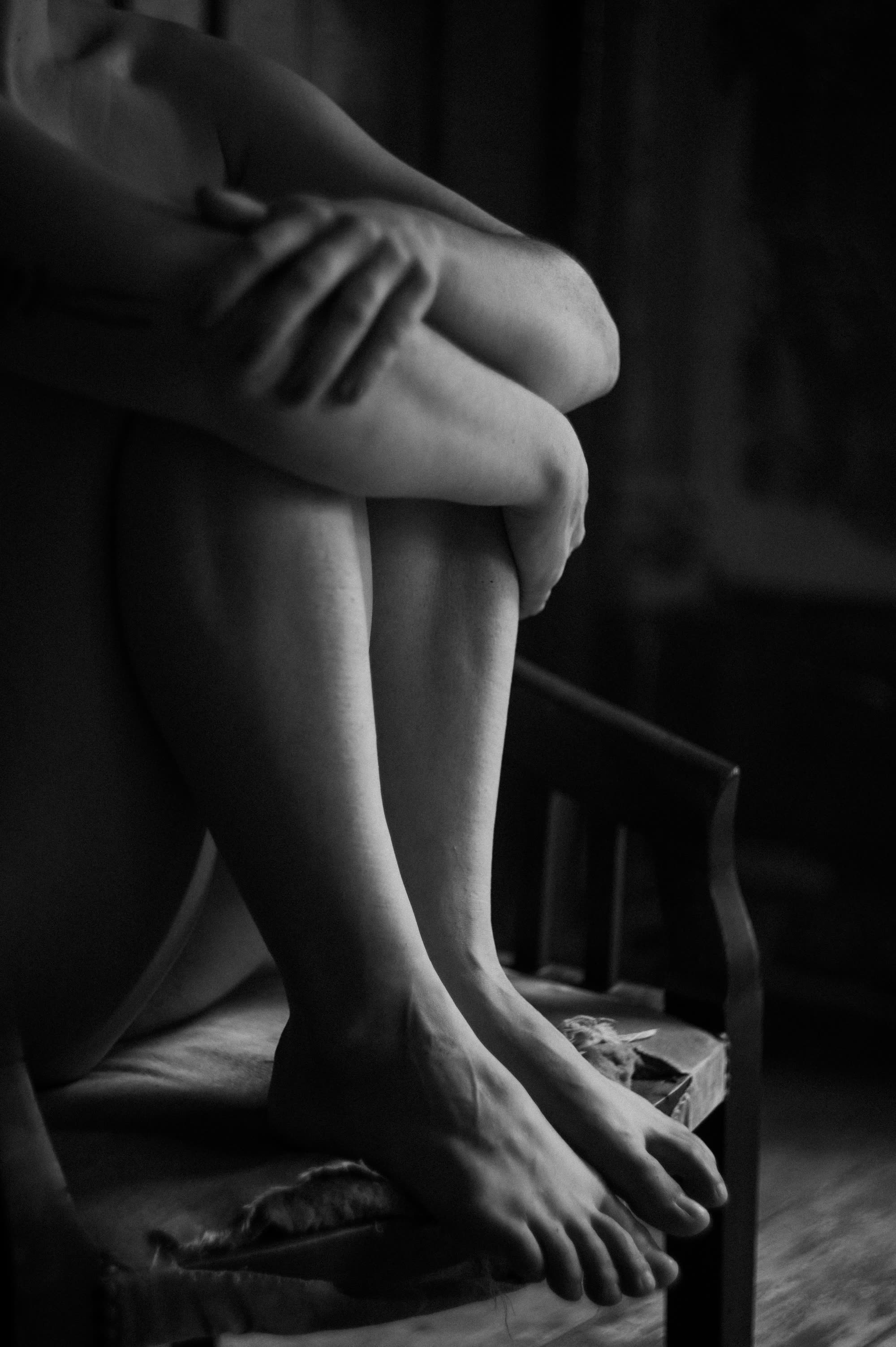 Close-up black-and-white photograph of crossed legs and clasped hands