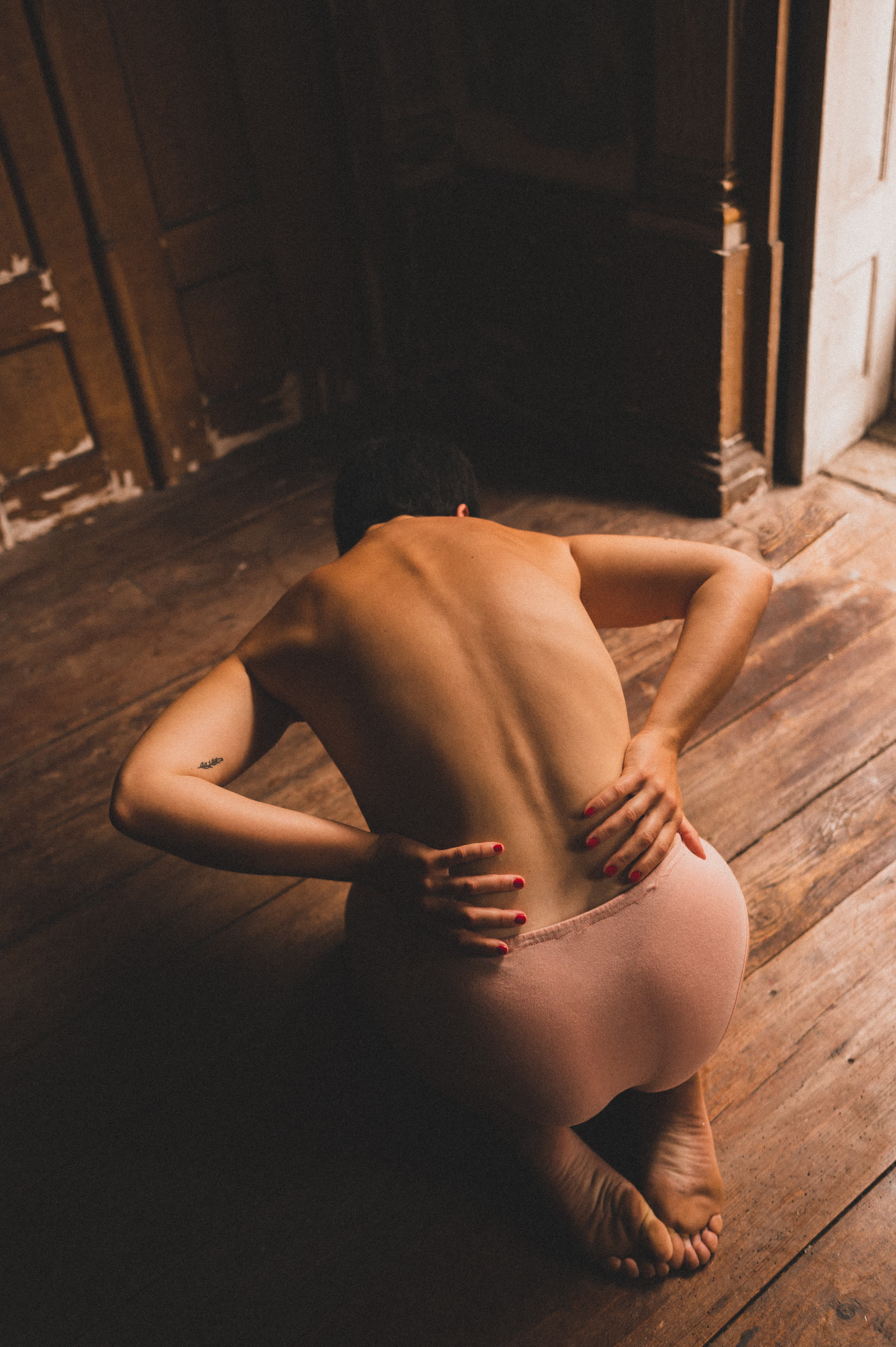 Juliana Fernandes kneeling on a wooden floor, back to camera