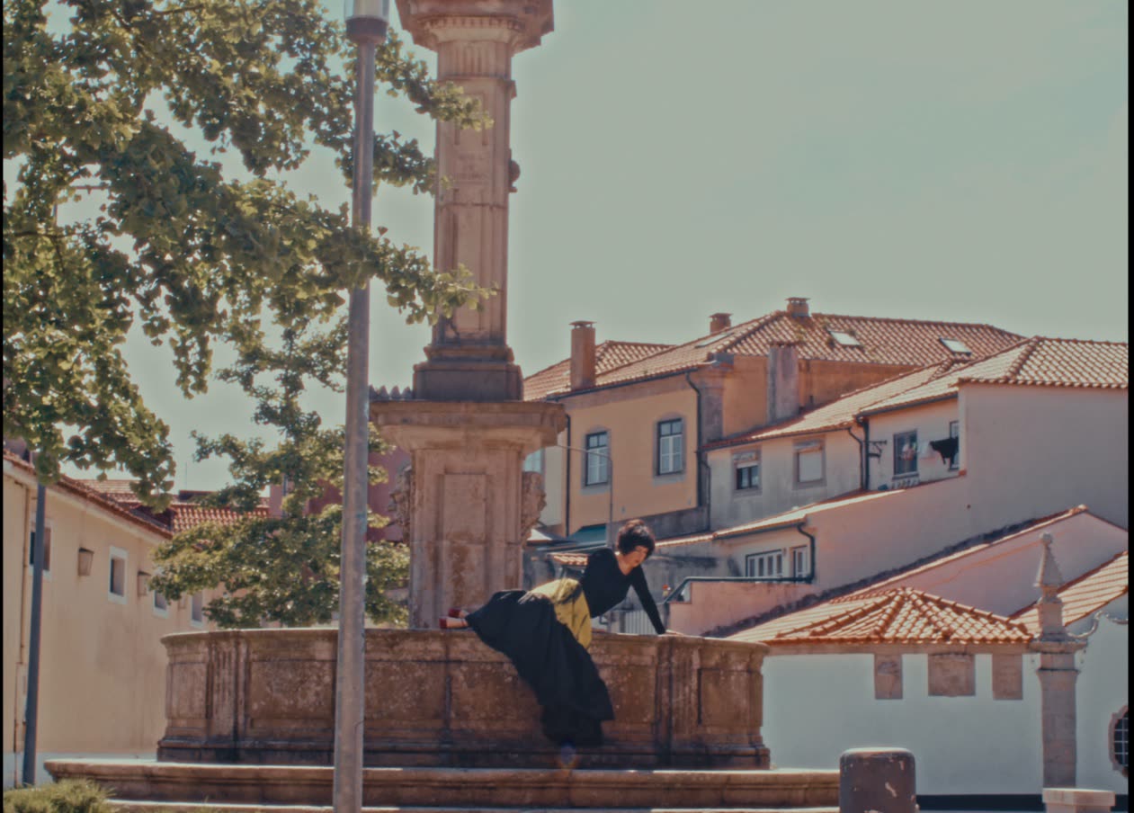 Dancer beside a stone monument in a town square, Em Quanto Espero