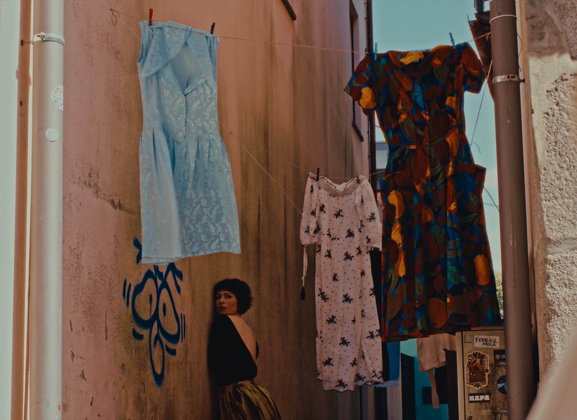 Colourful dresses hanging against a weathered wall, Em Quanto Espero