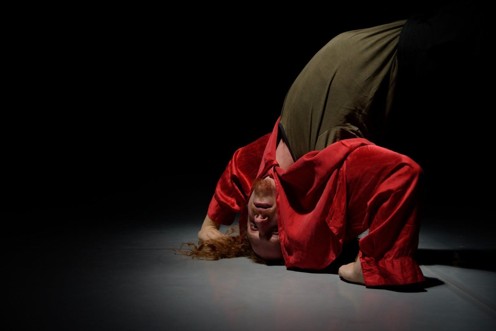 Performer curled on the floor in a red costume, Everyours