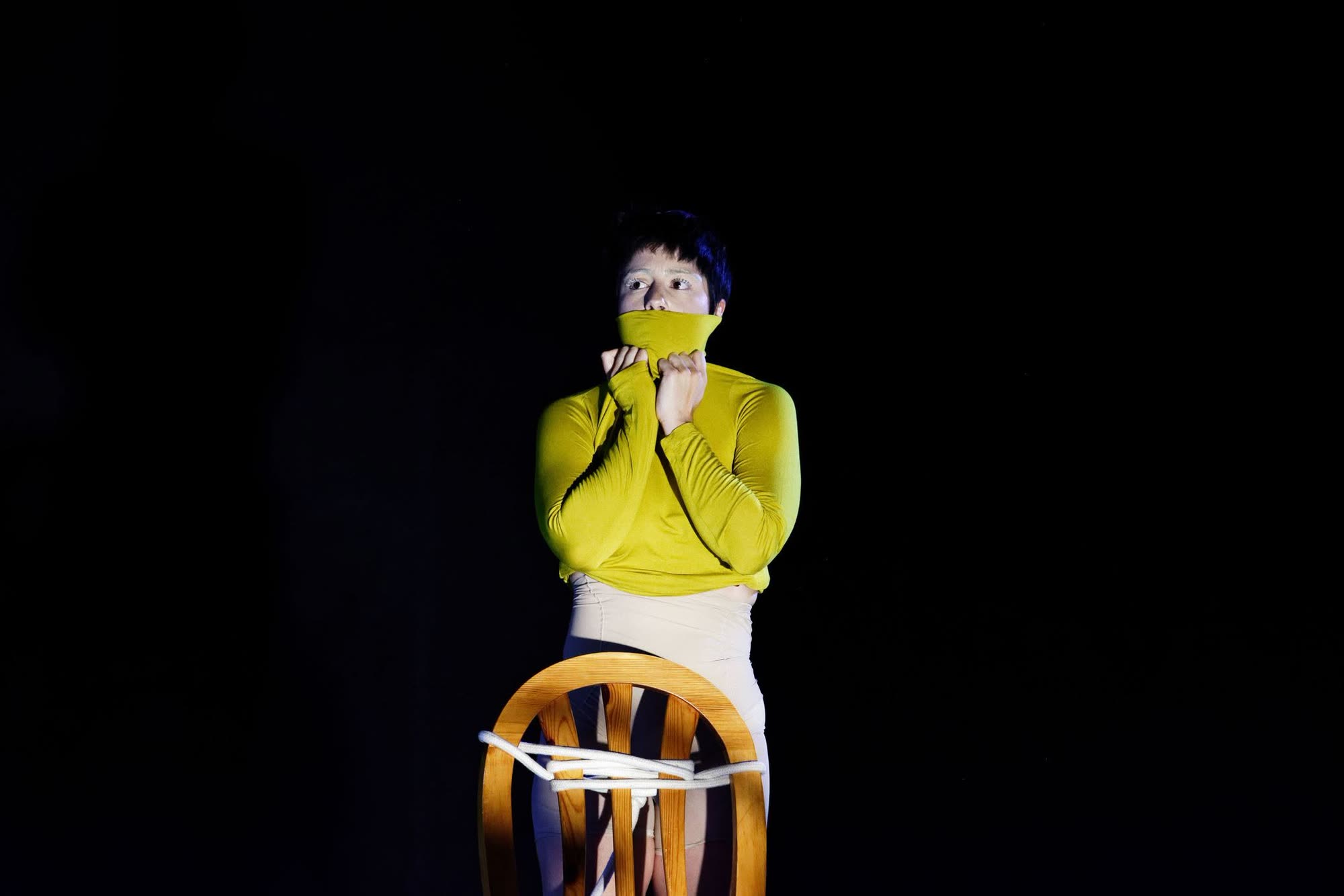 Performer in a yellow costume tied to a chair, In the Absence of Tenderness