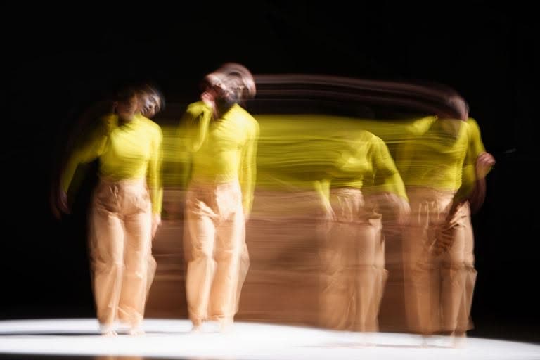 Long-exposure image of a performer in motion in a yellow costume, In the Absence of Tenderness