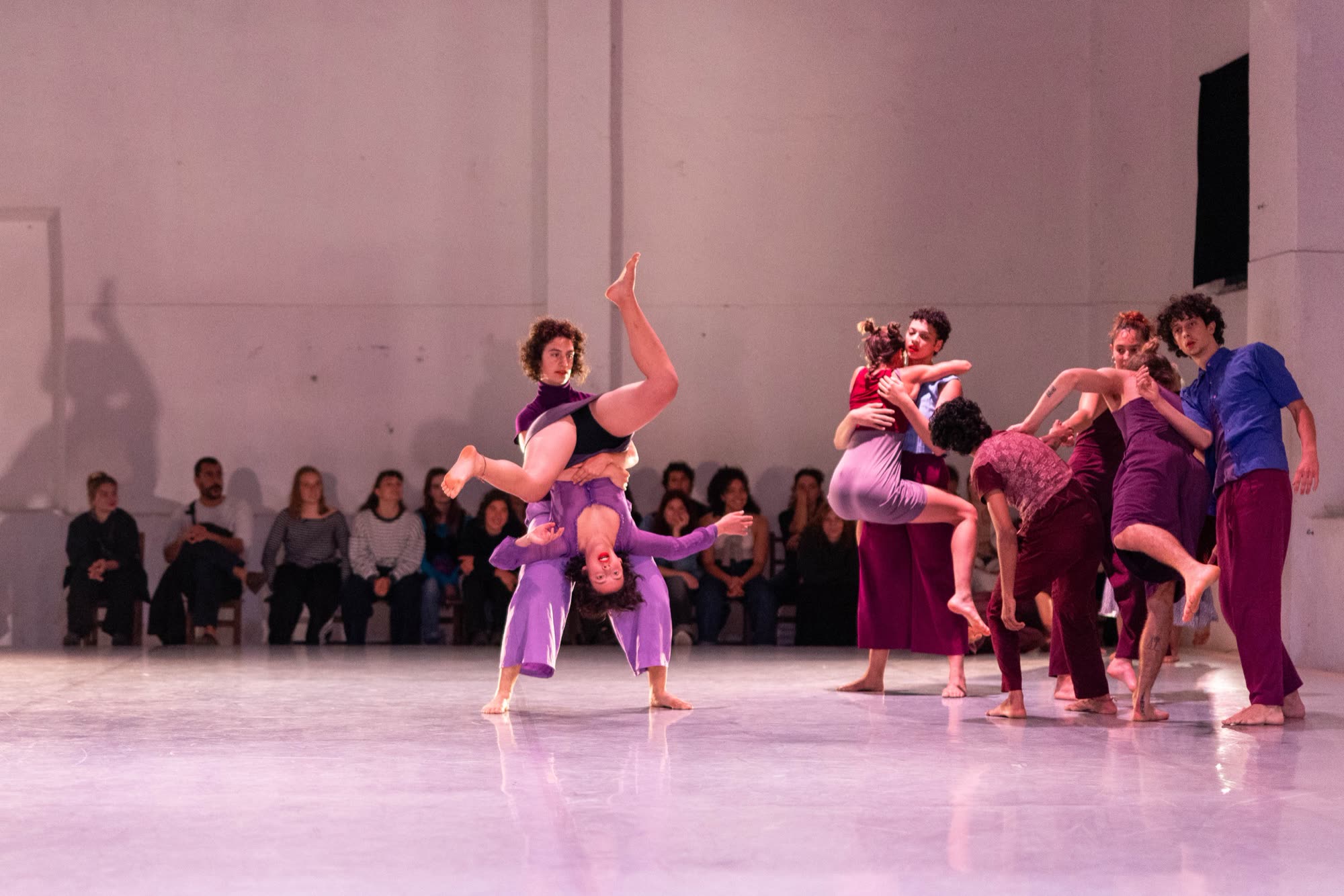 Group of performers in purple huddled on stage, Revoada
