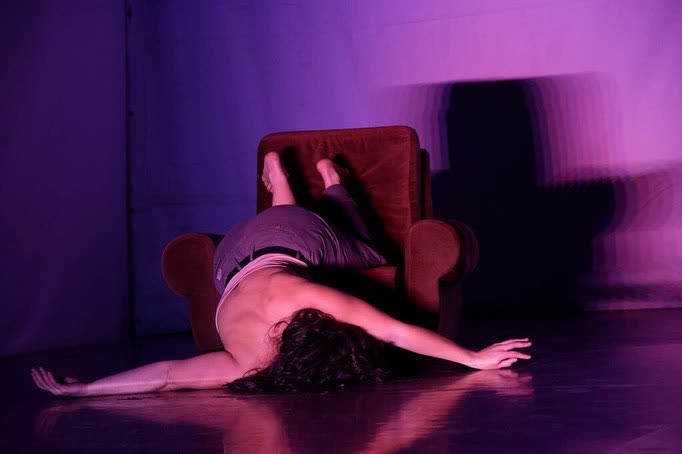 Performer lit in purple beside a chair on stage, When the Bells Don't Chime